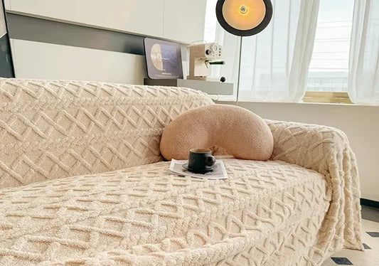 Couverture Smile ultra douce posée sur un canapé 3 places dans un salon chaleureux, ambiance cocooning hivernale. Décoration intérieure