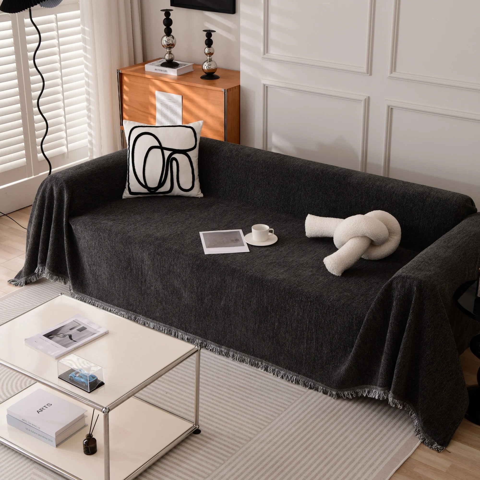 Housse de canapé en chenille noir avec bordures à glands, posée sur un canapé moderne – idéale pour déco intérieure ou détente en extérieur
