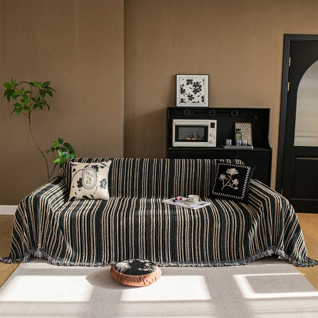 Housse de canapé en polaire Jacquard à rayures avec pompons, installée sur canapé en L dans salon lumineux et chaleureux. Décoration intérieure