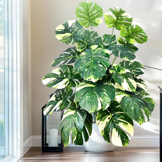 Plante artificielle Monstera 110 cm au feuillage vert luxuriant, posée dans un intérieur moderne avec mobilier bois et lumière naturelle